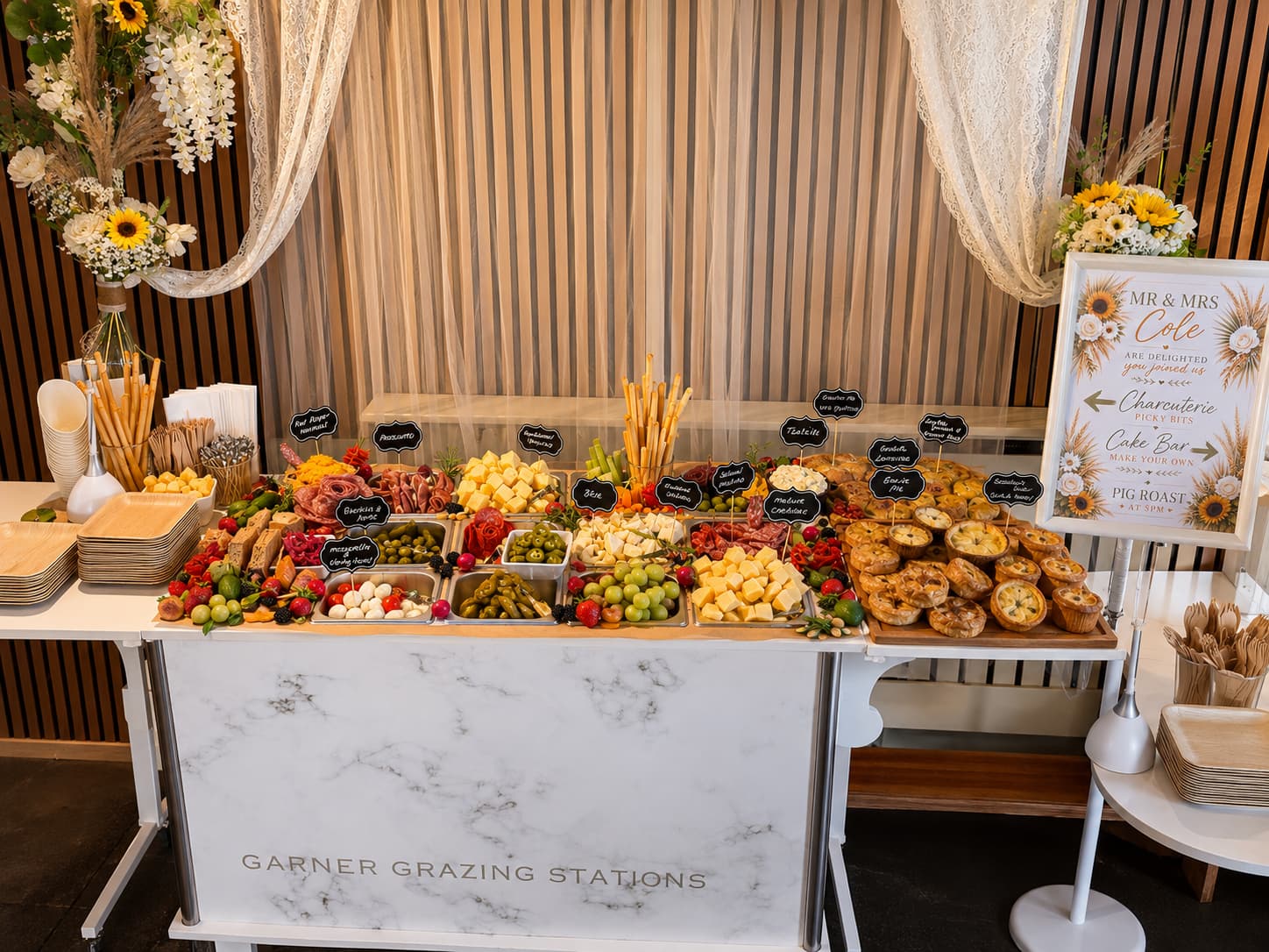 Elaborate wedding grazing station featuring meats, cheeses, fruits, and savory pies on a marble table.