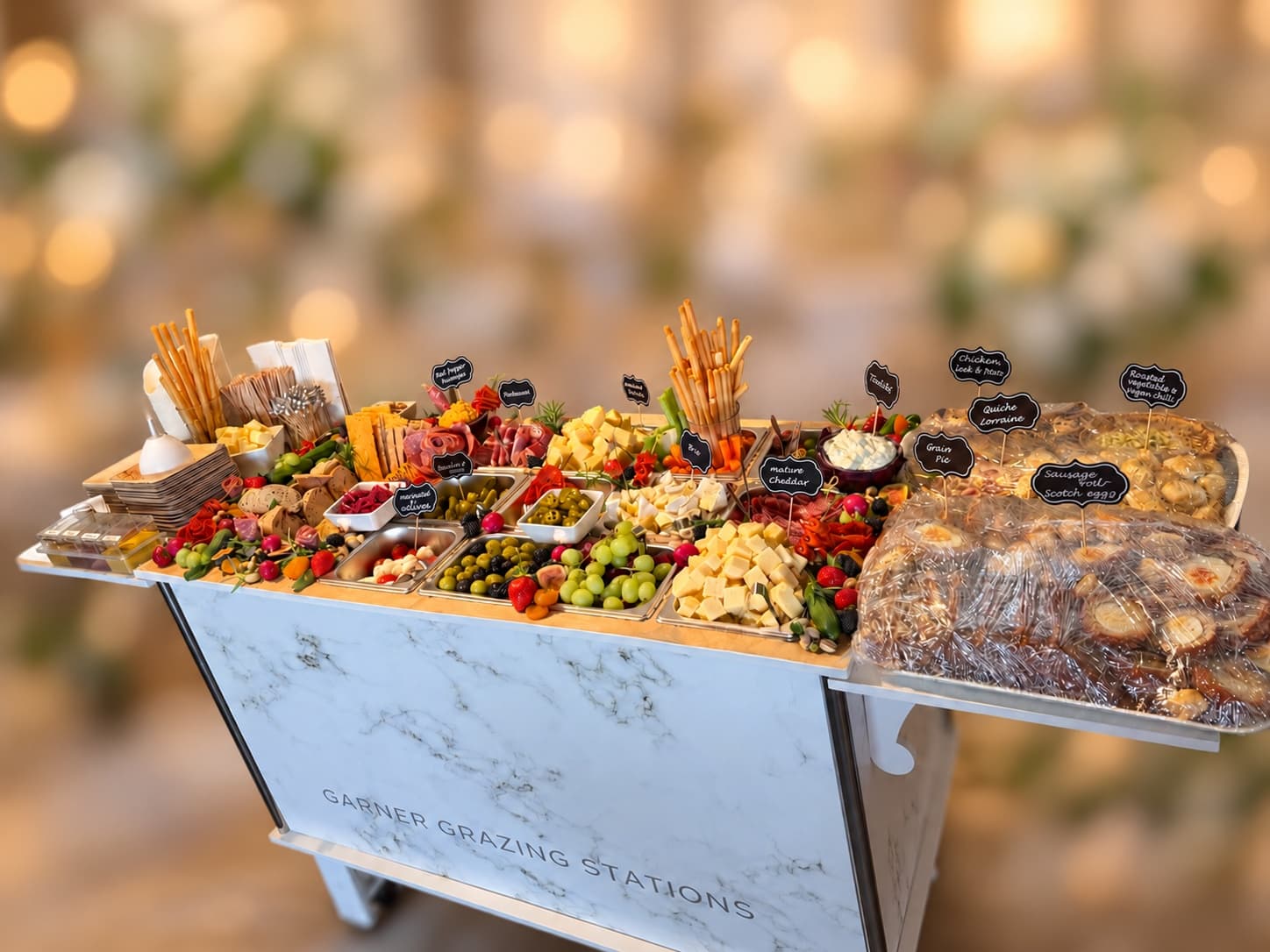 Marble grazing station cart featuring an abundant spread of cheeses, meats, and savory snacks.