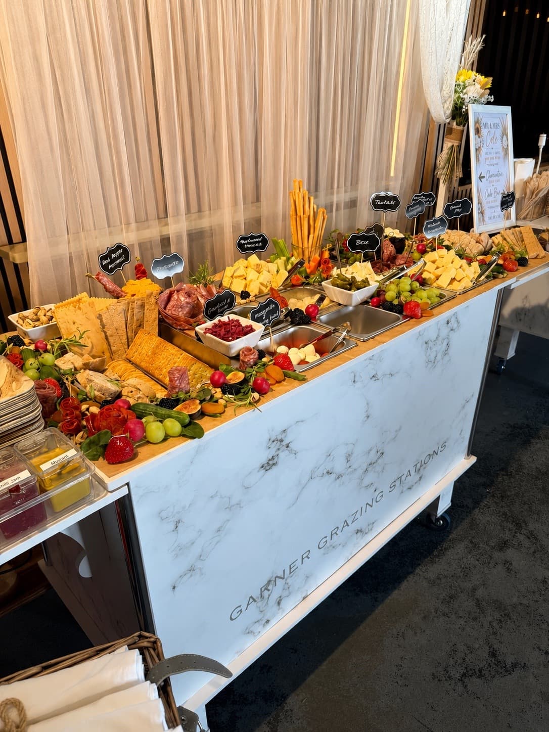 Elaborate grazing table on a marble cart with assorted cheeses, meats, crackers, and fresh fruit.